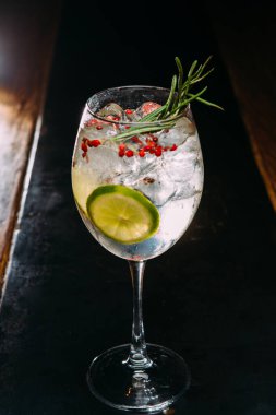 Ferahlatıcı cin ve tonik kokteyli limon dilimi, taze biberiye filizi ve kırmızı biber taneleriyle süslenir.