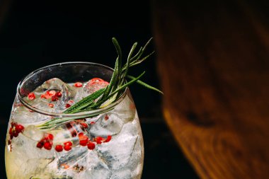 Taze biberiye ve pembe biberiyelerle süslenmiş cin ve tonik kokteylin yakın plan çekimi canlandırıcı ve ferahlatıcı bir içecek oluşturur.