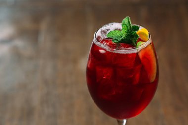 Serinletici kırmızı kokteyl buz, nane yaprakları ve bir dilim meyve ile süslenir. Kök bir bardakta kırsal ahşap bir masada servis edilir.