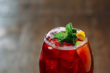 Buz küpleri, taze nane ve meyve dilimleri içeren canlı kırmızı kokteyl canlandırıcı ve görsel olarak çekici bir içecek yaratıyor.