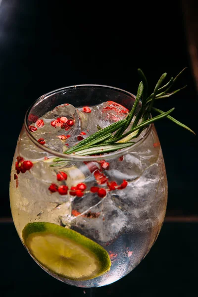 Cin ve tonik kokteyli taze biberiye filizleri ve pembe biberlerle süslenerek görsel olarak çekici ve lezzetli bir içecek yaratılıyor.