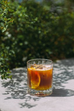 Refreshing cold brew coffee with an orange slice and spices in a glass, placed on a sunlit table outdoors