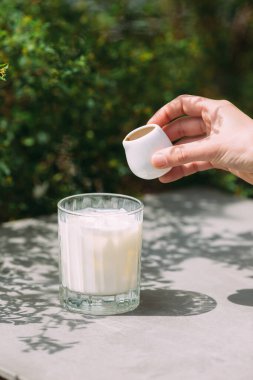 Küçük bir sürahiden espresso dökerek güneşli bir açık hava masasında bir bardak buzlu süte, kremalı, soğuk kahve tabakası oluşturur.