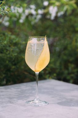 Refreshing cocktail with ice cubes and a slice of melon as garnish, served outdoors on a concrete table with green background