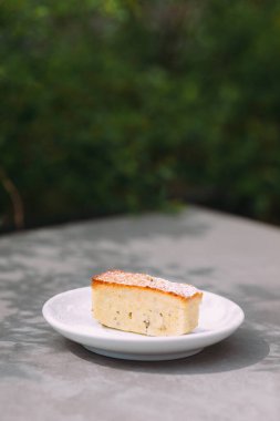 Pound cake slice with powdered sugar on a small white plate, enjoying a moment outdoors. Simple and sweet