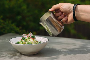 Metal sürahisinden kefir dökerek geleneksel Rus okroshka soğuk çorbasını otlar, sebzeler ve yumurta süsleriyle dolduruyorlar.