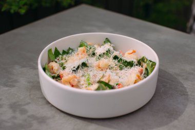 Flavorful shrimp salad served in a white bowl, featuring prawns, green leaves, and a generous sprinkle of parmesan cheese