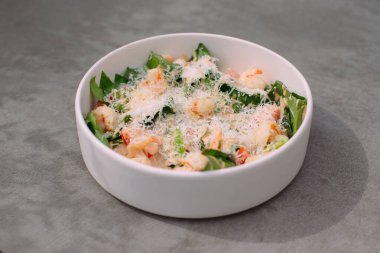 Shrimp and greens salad with creamy dressing and grated parmesan cheese in a white bowl, sitting on a gray surface