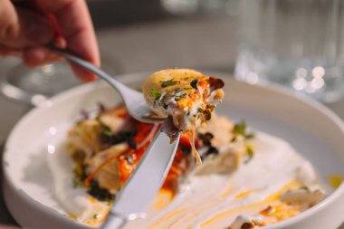 Lezzetli deniz mahsullü ravioli yiyen kişi çatal ve bıçaklı makarna, kremalı sos ve taze otlar yiyor.