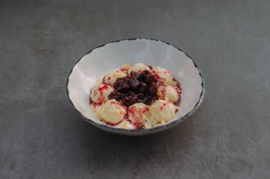 White ceramic bowl filled with cooked cottage cheese dumplings, topped with sour cherries, cherry sauce, and almond flakes
