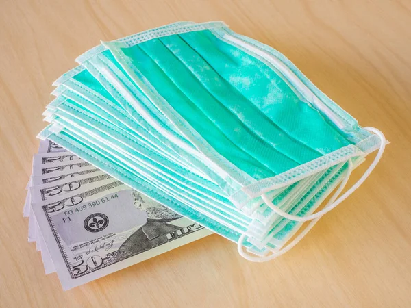 Tahta zemin üzerine izole edilmiş, hayran şekilli Amerikan para banknotlarına bir sürü tıbbi yeşil maske takılmış. Kişisel koruma için tıbbi malzeme aksesuarları kavramı. Yakın plan.