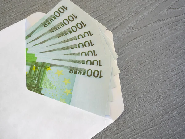 Close-up of Euro paper money in white envelope on a gray colour wooden texture background. A bundle of 100 Euro bills. Money received as a gift. The concept of bribery and black paycheck.