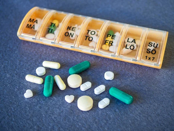 Close-up of seven day pill box with pills on blue background. A weekly box container of tablets, vitamins for routine treatment. Daily dosage of medication in orange pill dispenser.