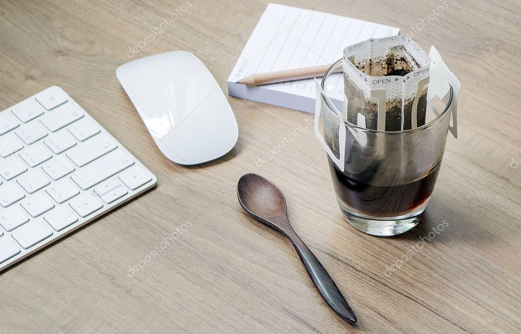 Instant freshly brewed cup of coffee or paper dripping bag on a cup on wooden table with computer keyboard and mouse