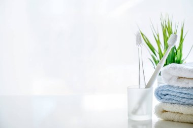 Beyaz zemin üzerinde yumuşak havlular ve diş fırçası, ürün gösterimi için kopyalama alanı.