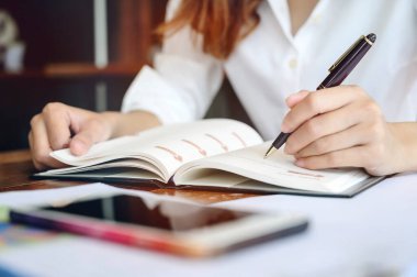 Yakın plan kadın eli kalem ve günlüğe yazı yazma, deftere yazı yazma ve ofiste çalışma.