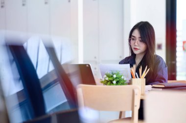 Dizüstü bilgisayar ve evrak işleriyle uğraşan genç bir kadın..