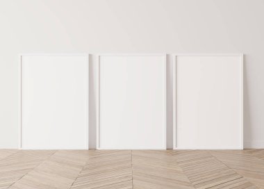 Beyaz ahşap çerçeve, ahşap zeminde duran üç poster.