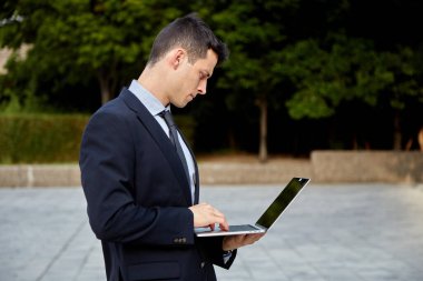 Sokakta dizüstü bilgisayarla çalışan genç bir yönetici..