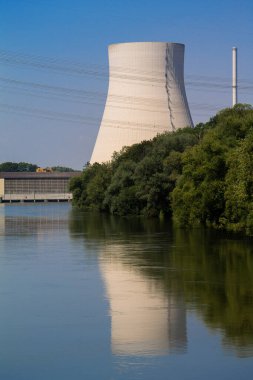 Bir nükleer santralin soğutma kulesi bir nehre yansıtılır. Önünde bir hidroelektrik santrali var. Her şey yakın plan..