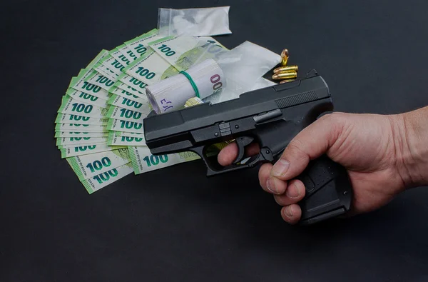 Gun, euro banknotes and drugs. The money opened and rolled. The drugs packed in bags. Individual 9 mm cartridges are included. The weapon is held in one hand.