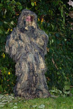 Kamuflajlı bir insan çitin önünde neredeyse görünmez olur..