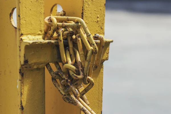 The old metal chain is coated with yellow paint and wound around a beam. Part of the fence in the courtyard of a residential building or in an industrial room in the open.