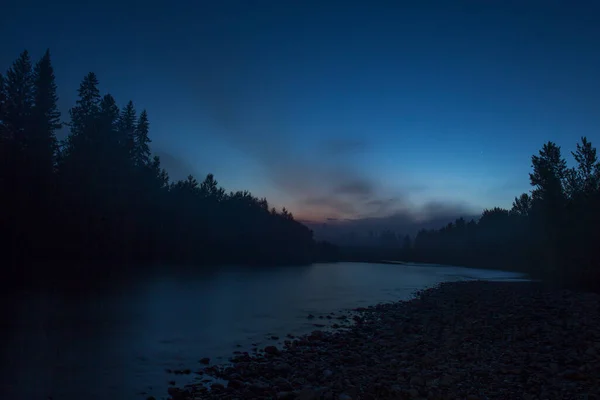 Night landscape: a small flat river, a dense coniferous forest and a pink sunset with clouds. Photos from a trip to Russia in the summer.