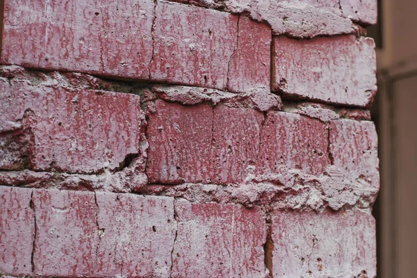 Part of the brick wall of the house is painted with pink paint. Texture: bricks and concrete.