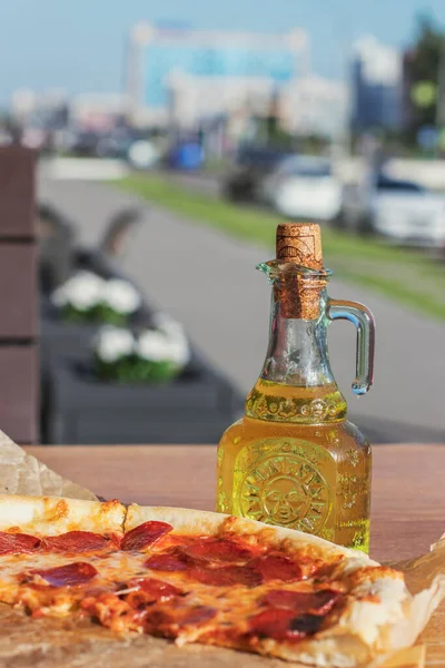 Street cafes have become popular in terms of COVID-19, people eat outdoors. Fragrant italian piperoni pizza and a bottle of olive oil in a restaurant against the backdrop of a city street.