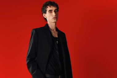 Pürüzsüz siyah giyinmiş, özgüvenli ve özgüvenli duran adam, zahmetsizce dikkat çekiyor..