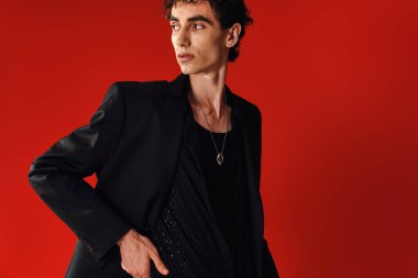 Zarif giyinmiş yakışıklı bir adam çarpıcı bir kırmızı arkaplan önünde güven içinde poz verir..