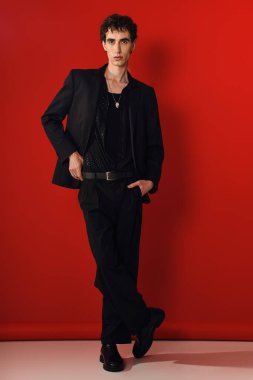 Şık giyinmiş yakışıklı bir adam dikkat çekici kırmızı bir arka planda, çekici bir şekilde poz verir..