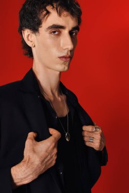 Zarif giyinmiş şık bir adam dikkat çekici kırmızı bir arka planla güven içinde poz verir..