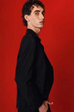 Şık bir adam şık bir elbiseyle cesur bir kırmızı zemine karşı güvenle poz verir..