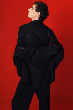 Bir adam, canlı kırmızı bir arka plana karşı, kendine güvenen bir şekilde dikiliyor..