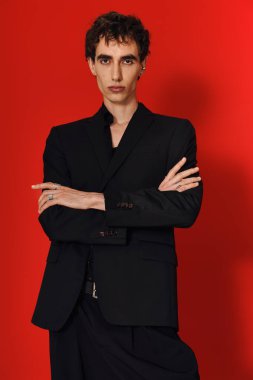 Yakışıklı bir adam kendine güvenerek kollarını kavuşturmuş siyah bir elbise içinde poz verir..