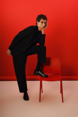 İyi giyimli bir adam düşünceli bir şekilde parlak kırmızı bir sandalyeye yaslanır, modern zarafeti göstererek.