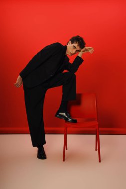 Yakışıklı şahıs şık giyinip dinamik bir poz verirken cazibe ve entelektüellik saçar..