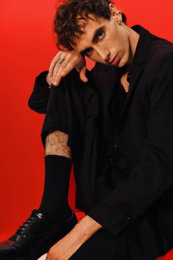 Zarif giyimli şık bir adam cesur bir kırmızı arka plana karşı özgüvenle poz verir..