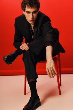 Yakışıklı bir adam göz kamaştırıcı bir arkaplana karşı parlak siyah bir takım elbiseyle poz verir..