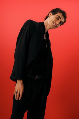 Zarif siyah elbiseli çekici bir adam büyüleyici bir şekilde kırmızı bir arka plana gülümsüyor..