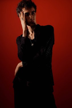 Şık giyinmiş yakışıklı bir adam, koyu kırmızı bir arka plana güvenerek poz verir..