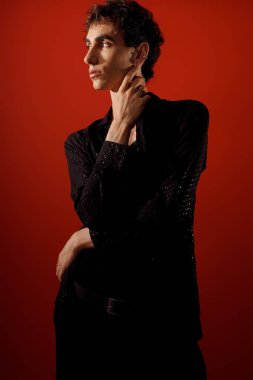 Şık bir adam zarif bir poz verir, çarpıcı kırmızı bir ortamda tarzını sergiler..