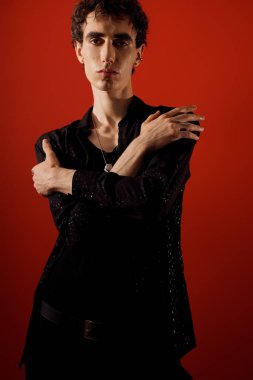 Zarif giyinmiş yakışıklı adam kollarını kavuşturup kendine güvenerek duruyor ve kendine has tarzını gösteriyor..