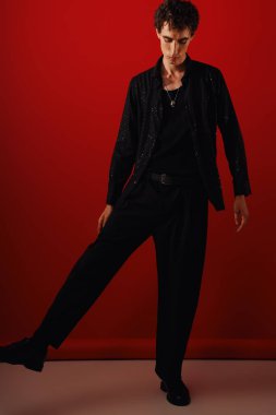 Yakışıklı bir adam stüdyo setinde dramatik bir şekilde poz verirken şık kıyafetlere güvenir..