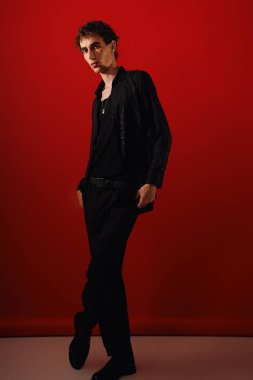 Zarif giyinmiş yakışıklı bir adam çarpıcı bir kırmızı arkaplan karşısında kendine güveniyor..