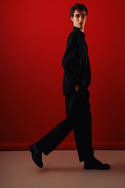 Şık bir adam şık giyinmiş, canlı kırmızı bir arka plana yakalanmış..