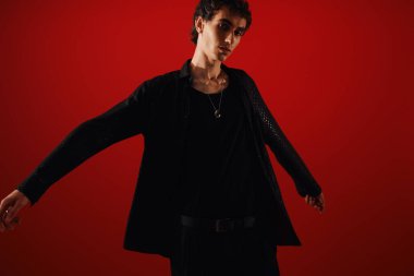 Parlak siyah elbiseli yakışıklı bir adam cesur bir duruş sergiliyor, kendine güveni ve çekiciliği var..