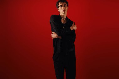 Şık giyinmiş şık bir adam cesur bir kırmızı arkaplan önünde güven içinde poz verir..